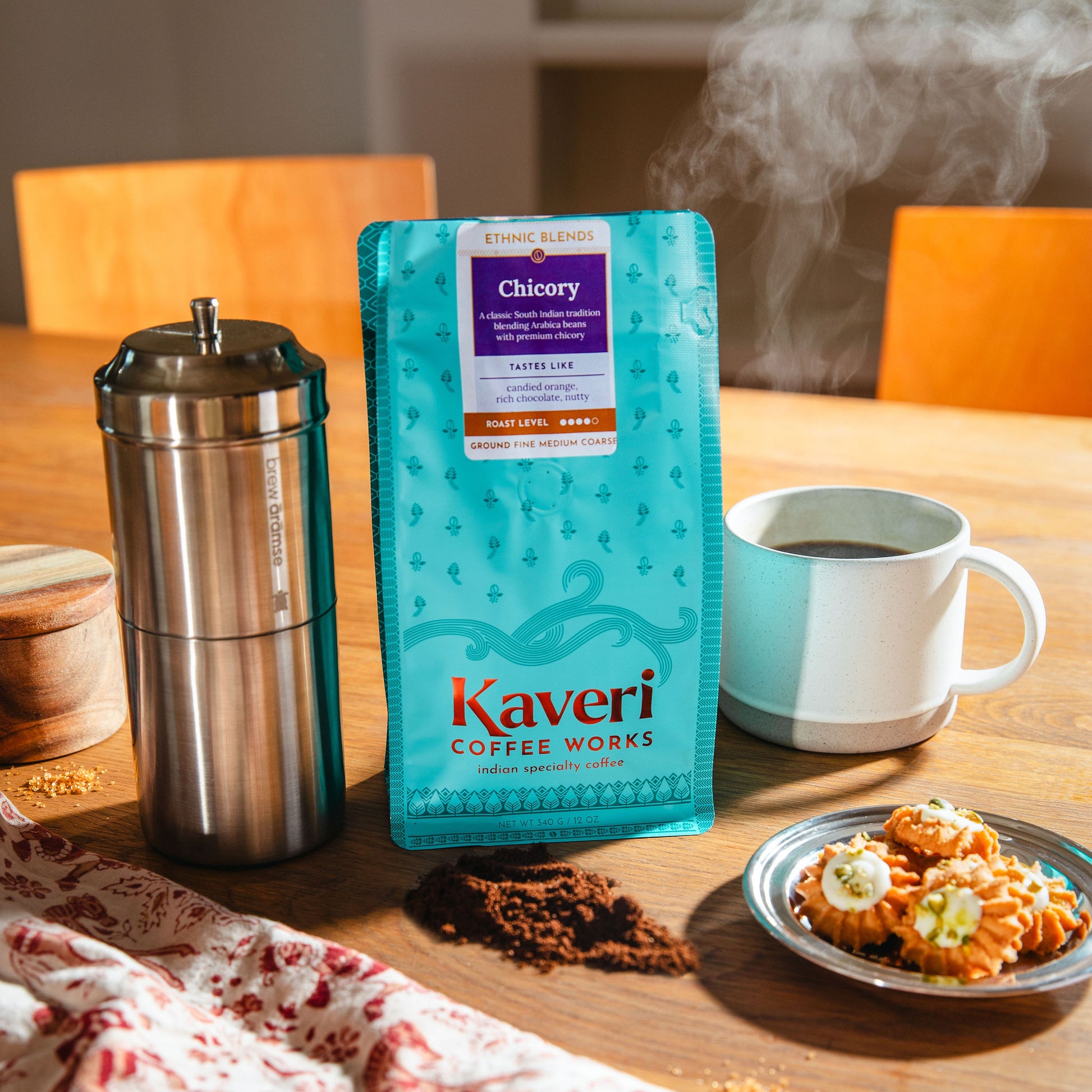 Kaveri Coffee Works Chicory coffee package on a table with a cup of coffee and cookies.
