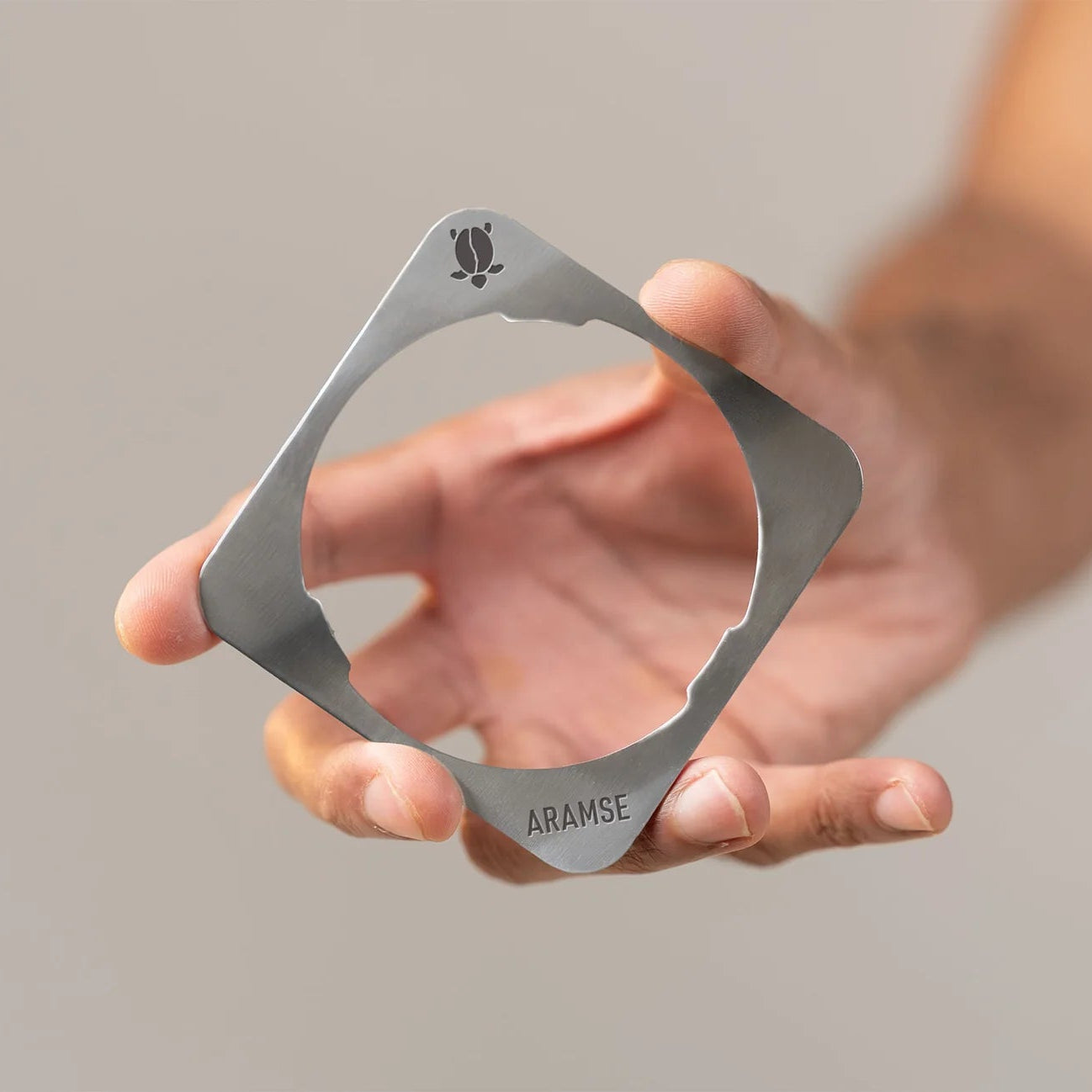 Hand holding a metallic bottle opener against a neutral background