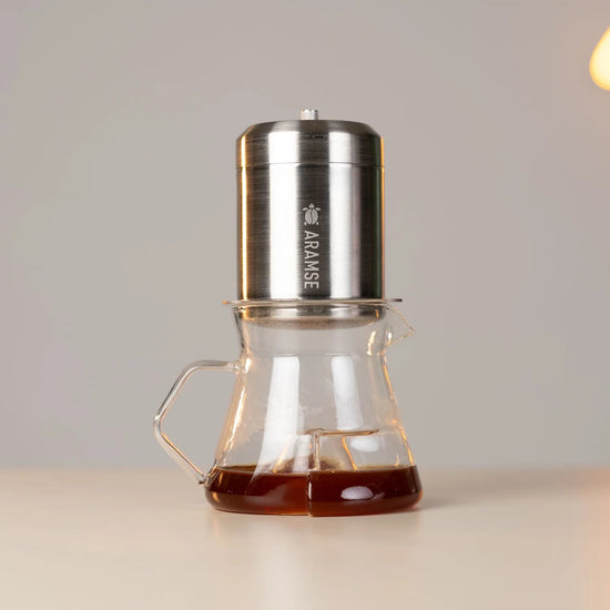 Coffee maker with glass carafe on a light surface, blurred lights in the background