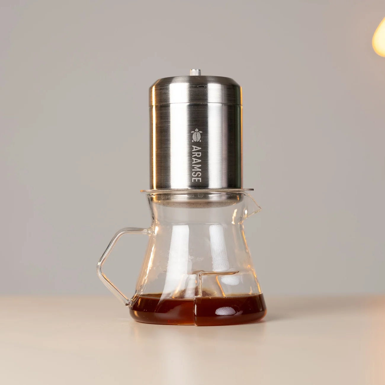 Coffee maker with glass carafe on a light surface, blurred lights in the background