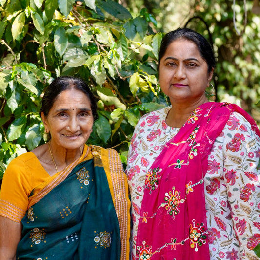 Two women in traditional sarees standing in front of green foliage
