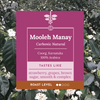 A product label for Mooleh Manay Carbonic Natural coffee, set against a background of green coffee leaves and small white flowers. The label is magenta pink with white text and a brown band at the bottom indicating roast level.