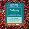 A coffee label card for 'Signature Collection' Peaberry Sweet & Spicy, set against a background of fresh red coffee cherries. The label features a dark teal background with white text and a light teal banner below, with a brown bar at the bottom indicating roast level.
